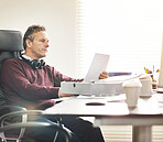 A businessman analysing paperwork in a modern office. A mature male executive going over a business document at his desk