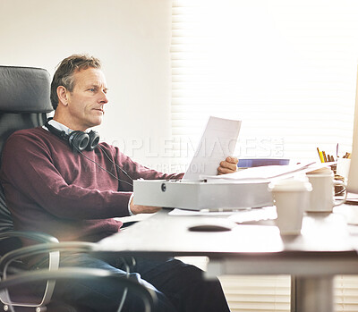 Buy stock photo A businessman analysing paperwork in a modern office. A mature male executive going over a business document at his desk