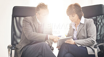 Buy stock photo Two colleagues using a tablet in a modern office. A mature businessman and businesswoman working online with a touchscreen, talking about business matters
