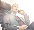 A businessman using a phone to make a call in a modern office. A mature male executive talking on his smartphone and working online with a digital tablet for business