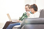 A mature couple using a laptop, relaxing at home. A happy senior man and woman in love browsing online with a computer on the couch
