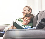 A mature couple reading a book and relaxing at home. A happy senior man and woman in love sharing a happy and comfortable moment on the couch