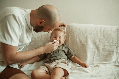 Buy stock photo Dad, child and wipe nose of sick kid on sofa in home living room, happy and smile for care. Father, boy and toddler with tissue for flu, allergies or covid, virus or disease, illness or cold in house