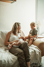 Love, bonding and mom with her toddler and baby relaxing on sofa in the living room of their home. Happy, sweet and young mother talking to her infant and newborn child with childcare in family house