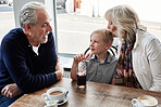 Senior man, woman and child in cafe, drink and soda with funny talk, vacation and relax with kiss. Grandparents, restaurant and boy with glass, tea cup and matcha with smile, laugh and conversation