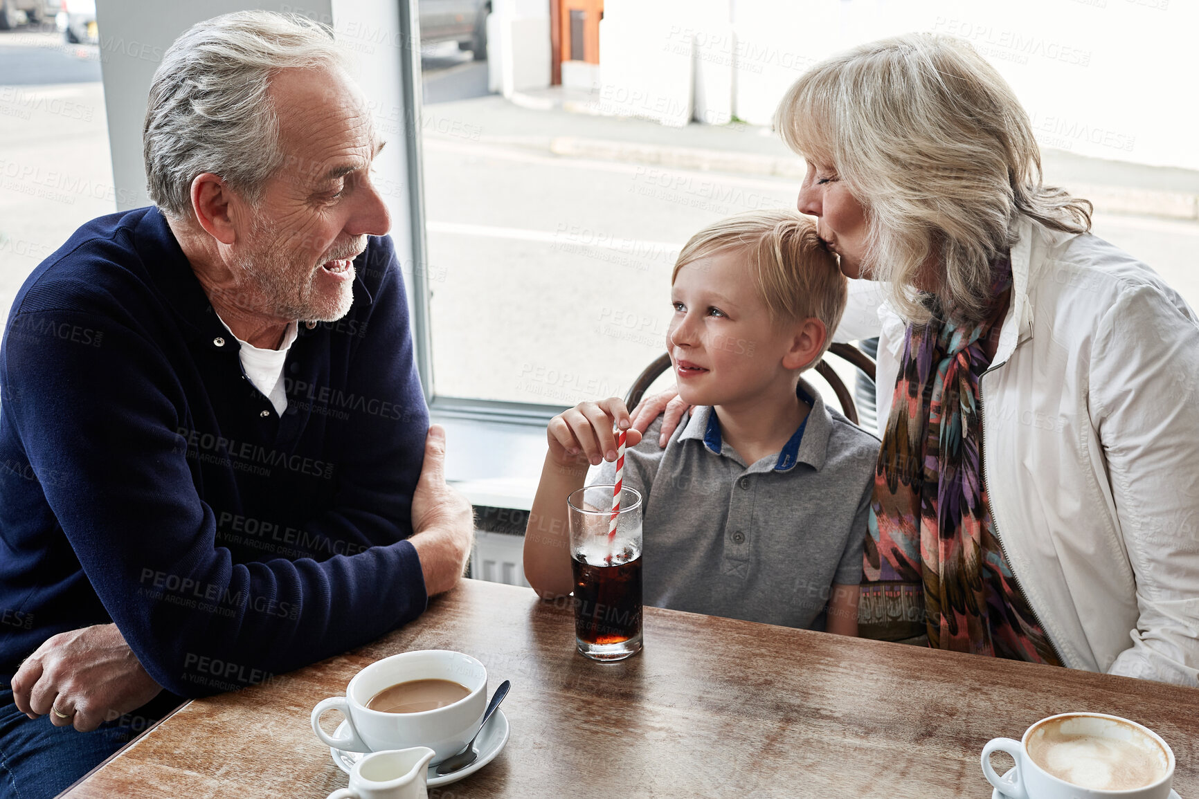 Buy stock photo Senior man, woman and child in cafe, drink and soda with funny talk, vacation and relax with kiss. Grandparents, restaurant and boy with glass, tea cup and matcha with smile, laugh and conversation