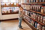Boy child, jar and candy in shop for gift, present and choice with thinking, dessert and sugar snack. Customer, kid and retail store with container for sweets sale, decision and shopping for discount