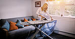 Woman, ironing and shirt on board in living room for housekeeping, domestic chore or cleaning with lens flare. Person, housewife and garment for iron, electric or appliance for satisfaction of fabric