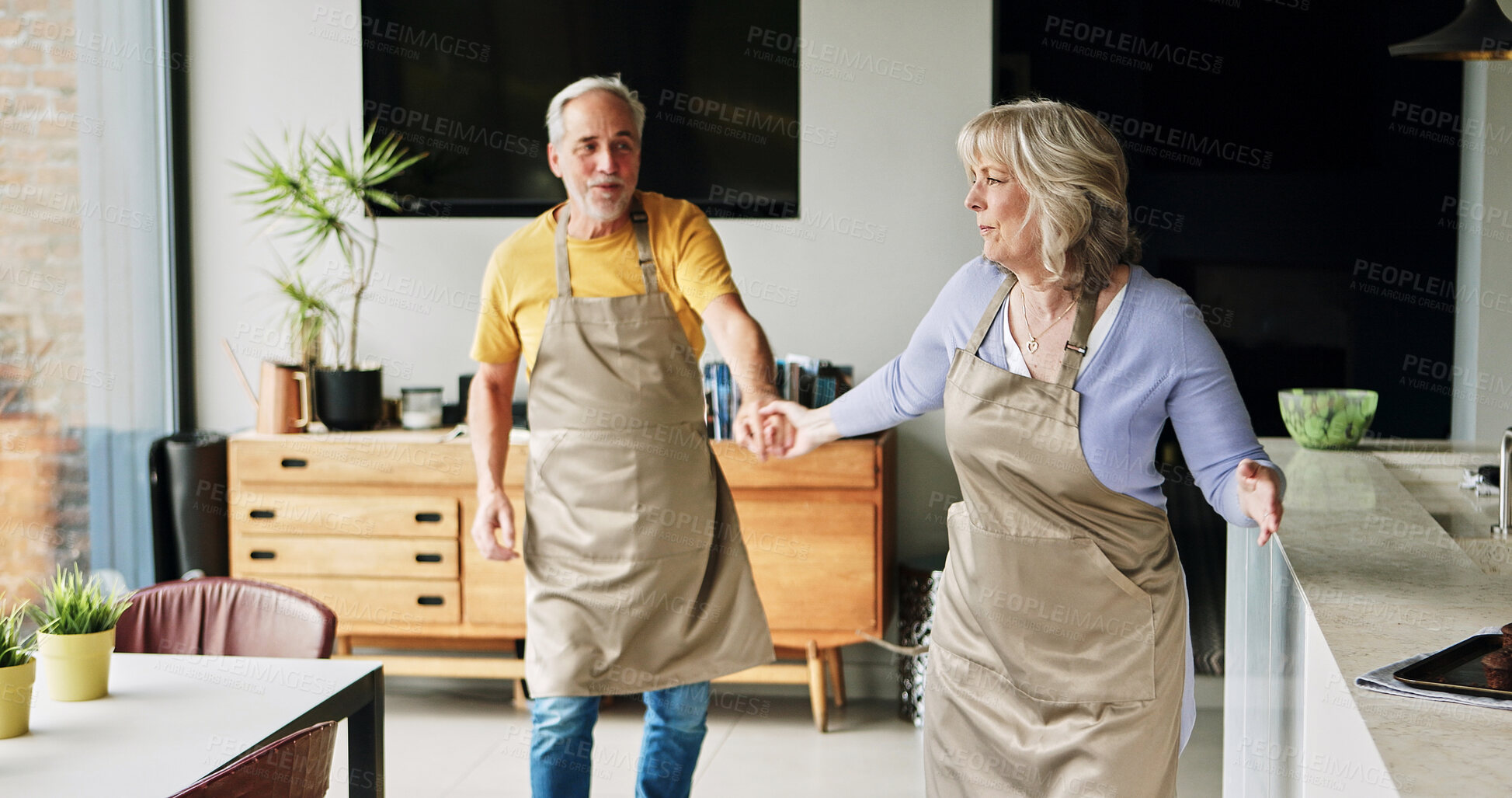Buy stock photo Senior, couple and dancing in living room or happy with bonding, retirement and marriage in apartment. Elderly, man or woman with dance for relationship, apron and romance with smile in house or home