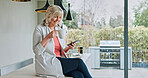 Old woman in kitchen, relax with coffee and phone, calm morning and sitting on counter to check social media. Home, breakfast drink and senior person with smartphone, networking and communication.