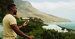 Phone, vacation and view with black man outdoor in nature for scenic holiday or travel to coast. Adventure, explore and journey with happy influencer person in mountain location for tourism review