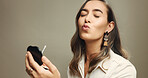 Woman, pout and lipstick in studio with beauty, funny and application with mirror by background. Person, model and playful with color, gear and eyes closed for cosmetic transformation with equipment