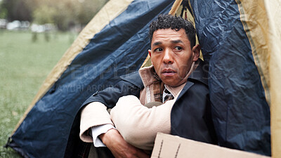 Buy stock photo Homeless, poverty and worry with man in park for depression, unemployment rate and crisis. Mental health, refugee and welfare aid with male person and sign in tent for tired, poor and thinking