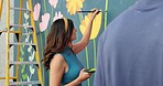 Woman, creative and painting in city for wall art, mural process or project to uplift community. People, team creativity or outdoor with paintbrush for floral design, volunteer collaboration or hobby
