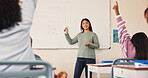 Teacher, children and raised hand in classroom, back and scholarship with answer, quiz and development at school. Woman, board and math for solution, question and education with learning at academy