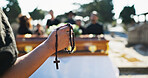 Funeral, hands and person with rosary, death and symbol for religious service, respect and graveyard. Outdoor, prayer and Christian with crucifix necklace for sermon, faith and gospel in cemetery
