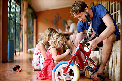 Buy stock photo Father, children and repair bicycle in home with help, support and DIY fix for kid development. Man, young daughters and bike in living room for remove training wheels, growth and family bonding