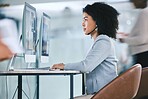 One focused young mixed race call centre telemarketing agent talking on a headset while working on a computer in an office. Female consultant operating helpdesk for customer service and sales support