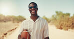 Smile, man and travel outdoor with football on vacation, holiday or adventure on dirt road. African person, tourist or relax in desert with ball for sports, trip or journey with sunglasses in Namibia