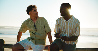 Buy stock photo Men, talking and friends at beach for break with bonding, communication and support outdoor. Conversation, people and happy on fence, travel or summer vacation to relax with connection in nature