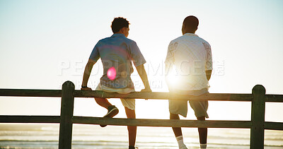 Buy stock photo Men, sunset and back of friends at beach for break with bonding, thinking and support outdoor. Conversation, people and flare by wood fence, travel or vacation to relax with connection in nature