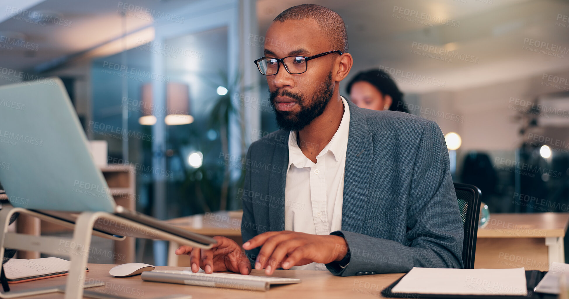 Buy stock photo African man, computer and typing at office, night and editing proposal with overtime at media company. Person, editor and writer by pc with glasses for deadline, project or time management at agency