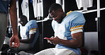 Football, player and texting with phone in locker room for message response, check notifications and game break. Sports, man and relax with smartphone for social media, online news and web connection