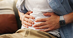 Stomachache, hands and person in home, pain and man with food poisoning in living room or indigestion. Abdominal, cramps and discomfort on couch, gas and bloating in lounge, diarrhea and constipation