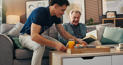 Buy stock photo Caregiver, elderly man and breakfast in home, reading and relax on sofa with book, food and kindness. Male nurse, senior patient and smile for meal with help, service and literature in retirement