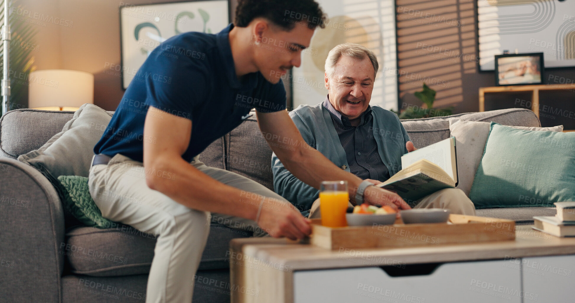 Buy stock photo Caregiver, elderly man and breakfast in home, reading and relax on sofa with book, food and kindness. Male nurse, senior patient and smile for meal with help, service and literature in retirement
