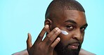 Portrait, cream and black man in studio, cosmetics and dermatology on blue background. African person, space and model with shine, creme and lotion with skincare, aesthetic and facial spf with glow