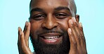 Portrait, man and hands for skincare in studio, healthy skin or moisturizer on blue background. Face, smile and grooming with African person apply cosmetics for dermatology and hydration facial