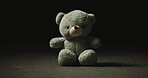 Night, shadow and teddy bear in studio for loss, isolation and forgotten toy on ground. Dark, floor and stuffed animal on black background for neglect, abandonment and unwanted with lost hope