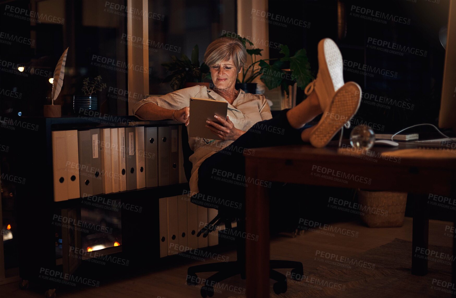 Buy stock photo Business, tablet and mature woman at desk with relax for notification, reading proposal or review. Night, online and employee with technology for information, email or news article in home office