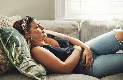 Buy stock photo Period, menstrual pain and a woman on a sofa in the living room of her home with cramps of the abdomen. Stomach, digestion or menstruation with a young female person holding her belly in discomfort