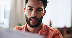 Reading, finance and man with documents in home for mortgage, loan payment and taxes. Worry, apartment and person with paperwork, bills and report for budget, financial planning and review savings