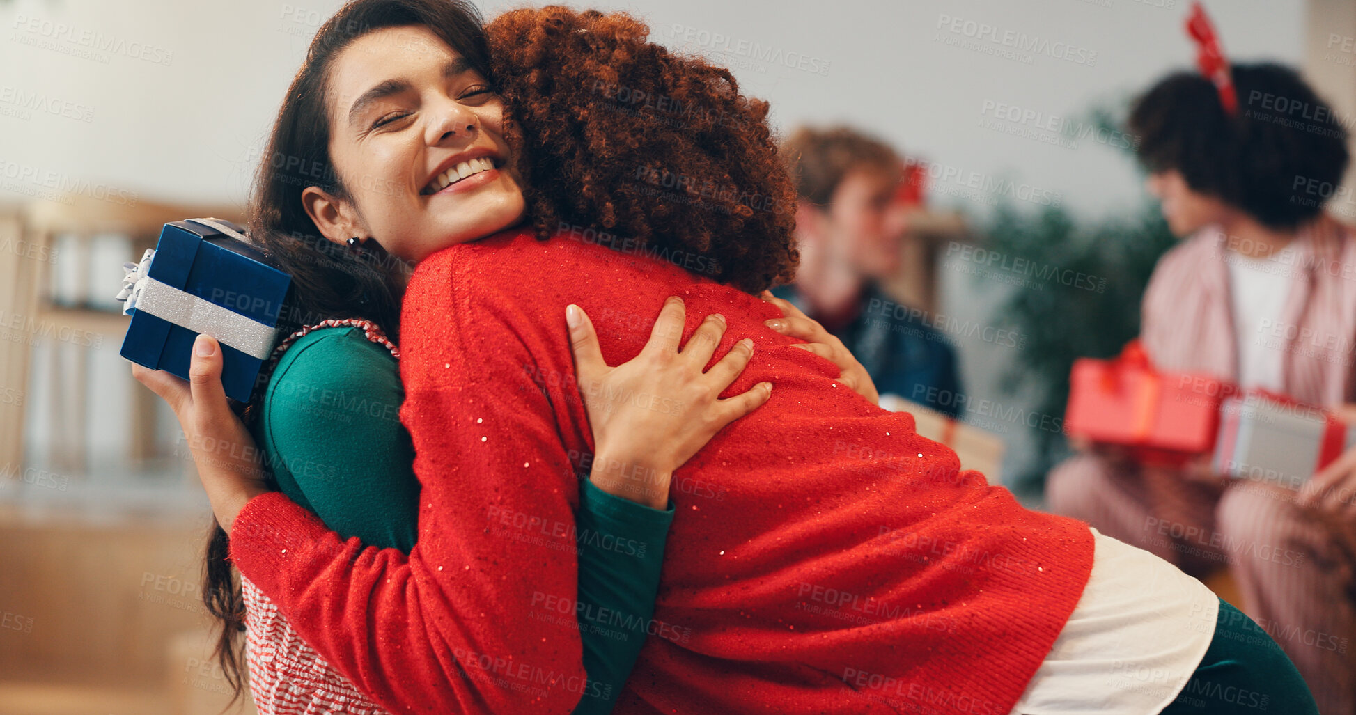 Buy stock photo Christmas, gift and hug with woman friends in living room of home together for celebration. Present, smile and thank you with happy people embracing at apartment for festive holiday in December