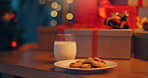 Christmas, cookies and milk on table in living room of home for celebration or December tradition. Biscuit, drink and presents with sweet food in apartment for culture, superstition or welcome