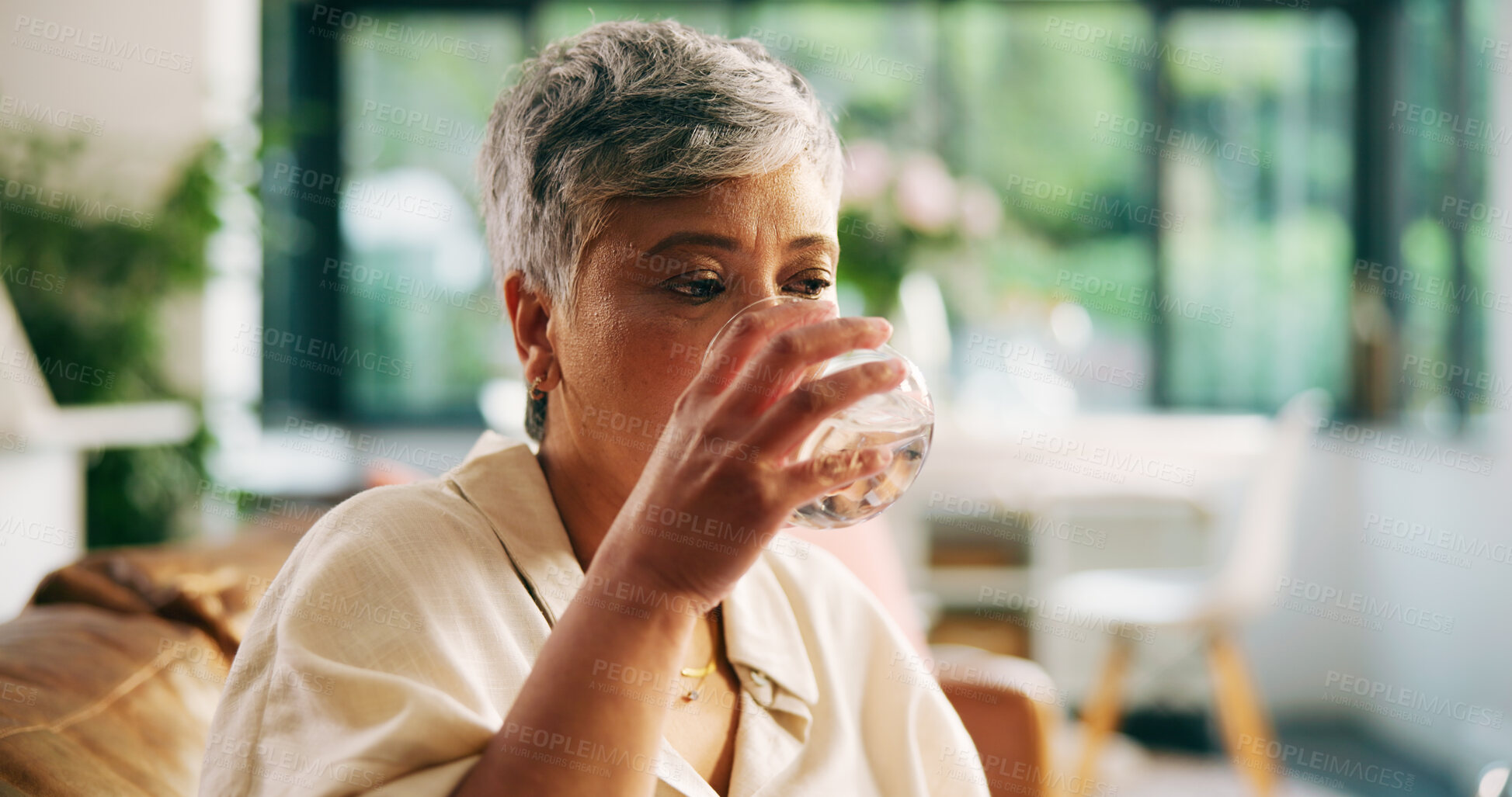 Buy stock photo Mature woman, drinking water and home on sofa, relax or hydration for wellness in living room. Person, glass and thirsty with liquid for nutrition, detox or gut health on couch in lounge at apartment