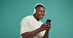Headphones, smile and black man in studio, cellphone or listening to music on green background. African person, space or mobile user with headset, audio or smartphone with sound, digital app or radio