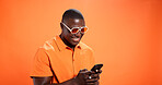 Black man, phone and smile in studio with chat, thinking and reading post on mobile app on orange background. Person, smartphone and notification with contact, scroll and choice on social network