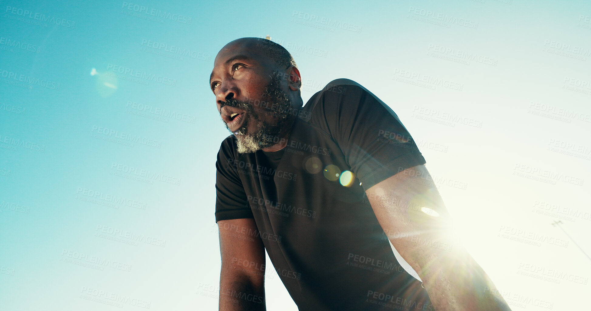 Buy stock photo Breathing, fitness and black man by blue sky for running, workout or training for marathon with break. Fatigue, lens flare and African mature athlete with rest for outdoor cardio exercise from below.