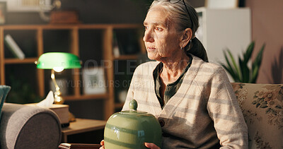 Buy stock photo Sad, old woman and thinking with urn in home for mourning, grief and loneliness in retirement. Loss, sorrow and senior person with depression in lounge for memory, bereavement and reflection of death