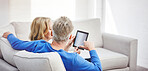 Mature couple browsing online on a digital tablet while relaxing together on a sofa at home