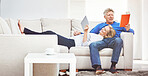 Mature man reading a book and mature woman browsing online on a digital tablet while relaxing together at home