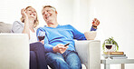 Happy mature couple drinking wine and eating popcorn while watching tv and relaxing together on a sofa at home