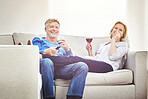 Happy mature couple drinking wine and eating popcorn while watching tv and relaxing together on a sofa at home