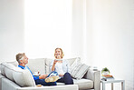 Mature couple drinking tea and eating sandwiches while having a conversation and relaxing together on a sofa at home