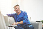Mature man browsing online on a laptop while relaxing alone on a sofa at home