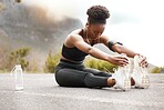 One african american female athlete with an afro listening to music on her earphones while exercising outdoors in nature. Dedicated black woman smiling while warming up before a workout outside